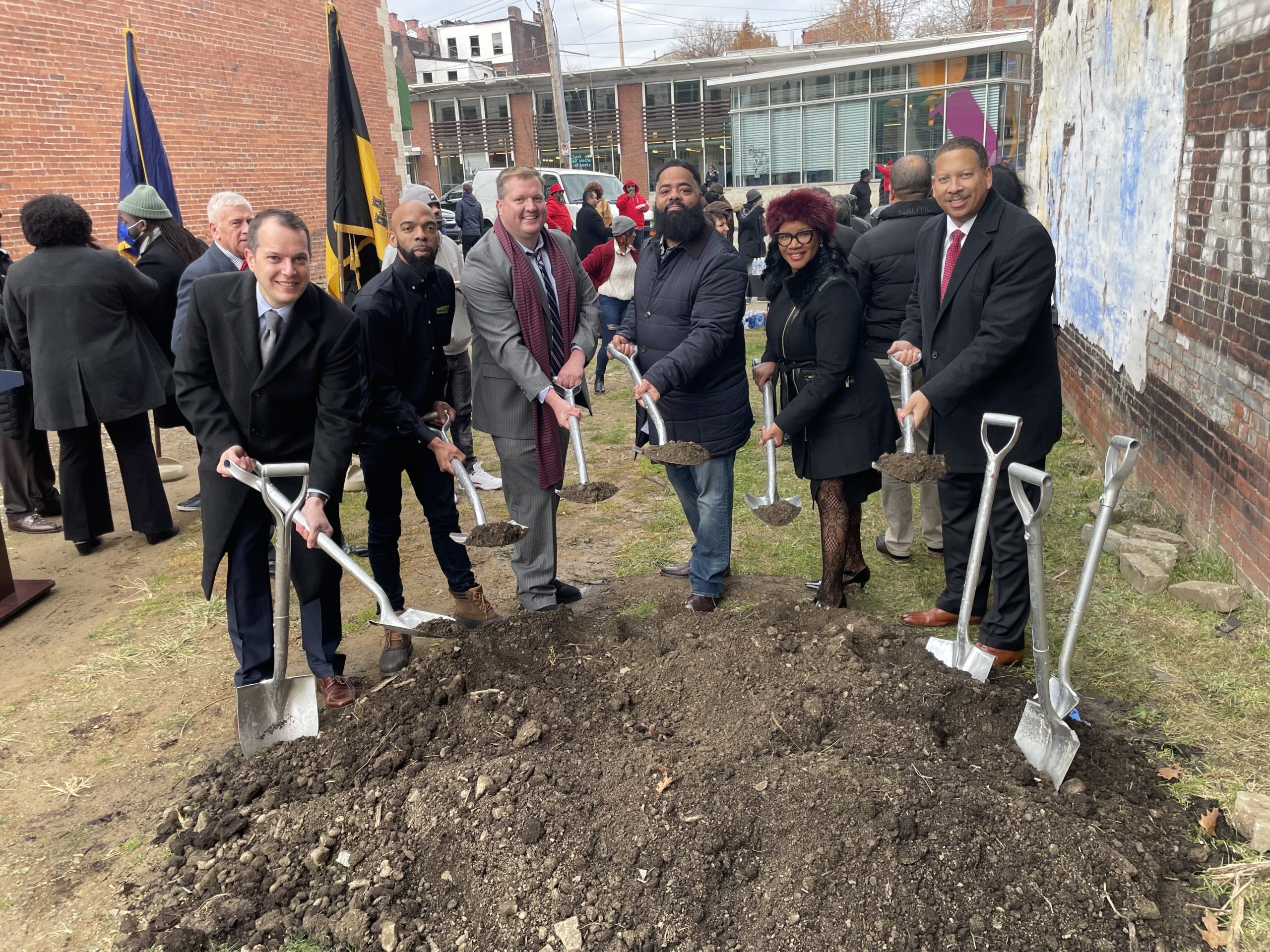 Image take at the groundbreaking of Big Tom's new building on Centre Avenue. People gathered around a pile of dirt, each holding a shovel full, to symbolize the official groundbreaking. Read caption for names.