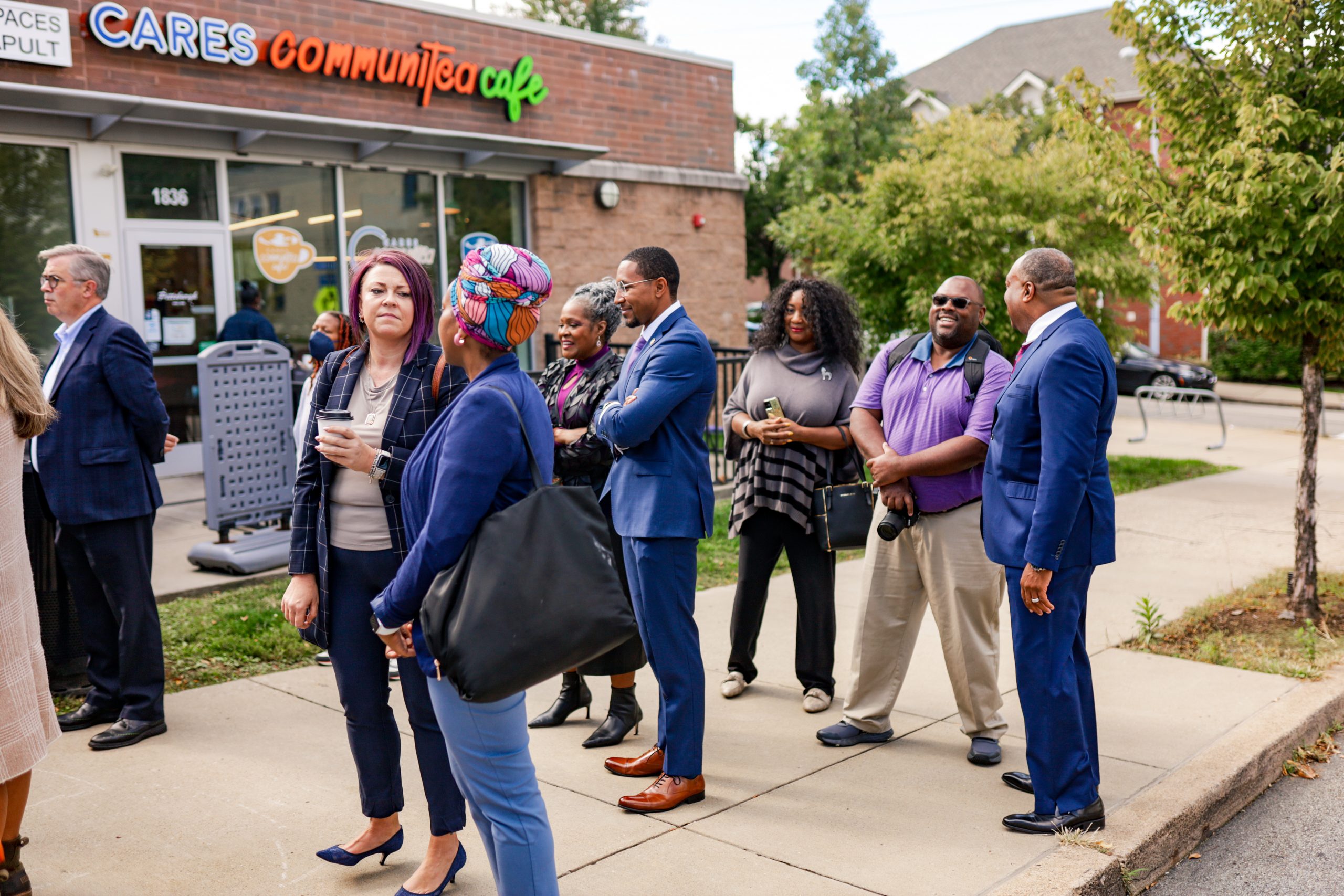 A crowd of people stand along a sidewalk at one of our press events. Behind them, you can see the entrance to the CARES Communitea Cafe in the Hill District.